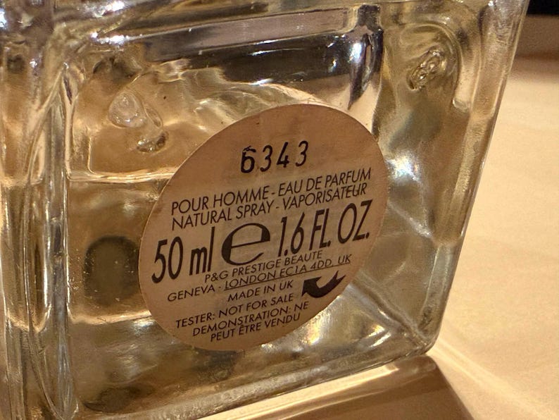 Puede incluir: Un frasco de perfume de vidrio transparente con una etiqueta beige. La etiqueta dice "POUR HOMME - EAU DE PARFUM NATURAL SPRAY - VAPORISATEUR" y "50 ml e 1.6 FL. OZ.". La botella est&aacute; marcada "TESTER: NOT FOR SALE".