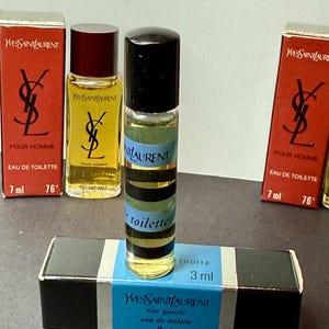 May include: A collection of Yves Saint Laurent miniature perfume bottles and boxes. The bottles are cylindrical with black caps and striped labels. The boxes are red and black with the Yves Saint Laurent logo and product information.
