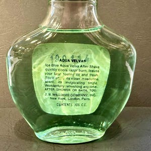 Puede incluir: Una botella de vidrio transparente de loci&oacute;n para despu&eacute;s del afeitado Aqua Velva con una etiqueta verde. La etiqueta incluye el texto "Ice Blue Aqua Velva After Shave" y otros detalles del producto. La botella contiene 105 ml.