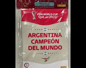 May include: A sealed Panini FIFA World Cup Qatar 2022 mega poster and 30 stickers pack. The packaging features a white and pink design with the text Argentina Campeón del Mundo, the official tournament logo, and a small graphic of a soccer player.
