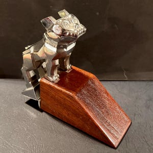 Può includere: Una statuetta di bulldog d'argento su una base di legno. Il bulldog è in piedi sulle zampe posteriori con le zampe anteriori sollevate. La base è in legno marrone scuro.