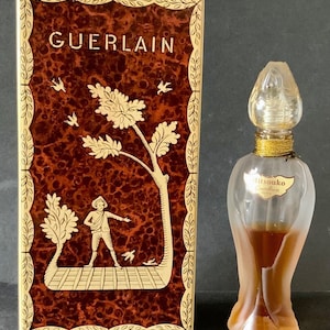 May include: A vintage bottle of Mitsouko perfume by Guerlain. The bottle is clear glass with a gold-coloured cap and a gold band around the neck. The bottle is filled with a light brown liquid. The box is rectangular with a gold border and a brown and gold design. The box has the word "Guerlain" printed in gold letters.