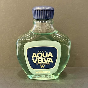 Puede incluir: Botella de cristal transparente de loci&oacute;n para despu&eacute;s del afeitado Aqua Velva. La botella tiene un tap&oacute;n azul oscuro y una etiqueta con las palabras "Aqua Velva" en letras doradas sobre un fondo azul oscuro. Contiene un l&iacute;quido verde claro.