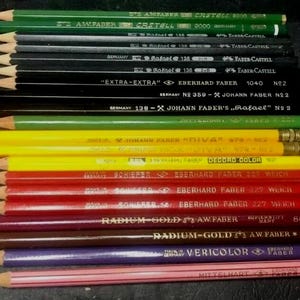 May include: A close-up of a collection of coloured pencils with various brand names and labels, including "Eberhard Faber", "Johann Faber", "Castell", and "Radium-Gold".