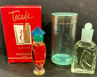 Puede incluir: Tres frascos de perfume en miniatura, todos de vidrio transparente con tapas de diferentes colores. Los frascos están etiquetados con "Rochas Paris" y "Tocade Eau de Toilette".