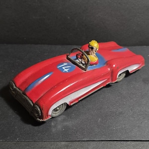Könnte beinhalten: Rotes und weißes Spielzeug-Rennwagen mit der blauen Nummer 14 an der Seite. Das Auto hat eine Fahrerfigur mit gelben Haaren und Sonnenbrille.