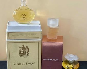 May include: A collection of vintage perfume bottles and boxes. The bottles include "L'Air du Temps" and "Premier Jour" by Nina Ricci. The boxes are beige and brown with gold lettering and illustrations. The perfume bottles are various shapes and sizes.