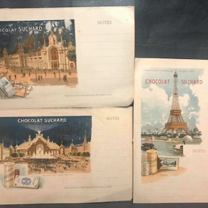 May include: Three vintage postcards advertising Chocolat Suchard, a Swiss chocolate brand. The postcards feature images of the Eiffel Tower, the Palace of Fine Arts, and the Palace of Electricity from the 1900 Paris World's Fair.