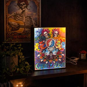 May include: A colorful Grateful Dead light-up sign featuring the band's iconic skull logo, dancing bears, and floral elements. A vintage poster is in the background. A record player is on a shelf below.