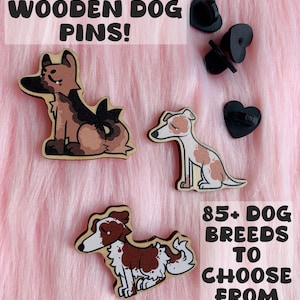 May include: Wooden dog pins featuring a German Shepherd, Greyhound, and Border Collie. The pins are brown, tan, and white, with black pin backs. Text reads "WOODEN DOG PINS!" and "85+ DOG BREEDS TO CHOOSE FROM."