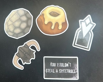 May include: A collection of five stickers featuring a gray stone, a brown sweetroll with white icing, a white geometric emblem, a dark horned helmet, and a rectangular black sticker with the white text YOU WOULDN'T STEAL A SWEETROLL.