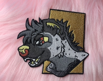 May include: Embroidered patch featuring a stylized hyena head with black, gray, and tan colors. The hyena has a detailed design with visible teeth and a red nose. The patch is set against a gold rectangular background.