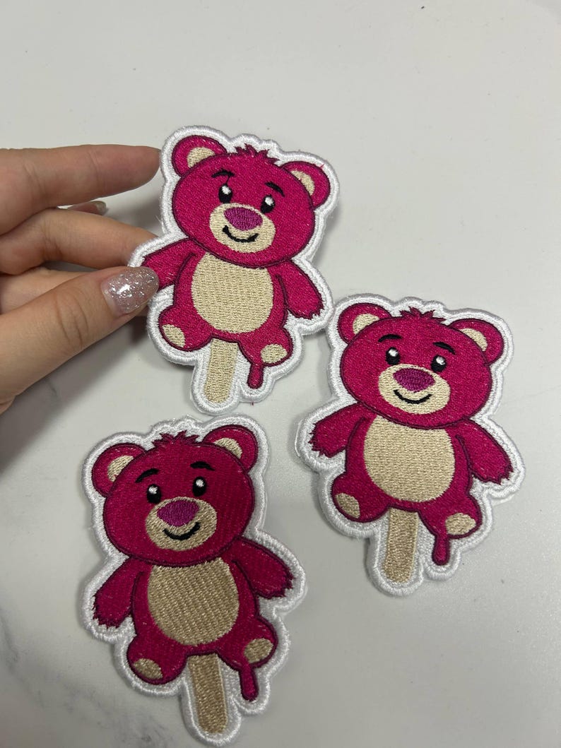 K&ouml;nnte beinhalten: Gestickte Aufn&auml;her mit einem rosa Teddyb&auml;r-Design mit hellbraunem Bauch und einem Eisstiel. Die Aufn&auml;her haben einen wei&szlig;en Rand und eignen sich f&uuml;r Kleidung oder Accessoires.