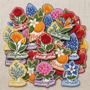 May include: A collection of embroidered patches featuring state flowers and city names. The patches showcase vibrant colors, including red roses, orange poppies, and bluebonnets, with text such as "California" and "New York".