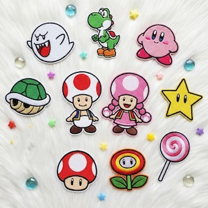 以下が含まれることがあります： スーパーマリオのビデオゲームシリーズのキャラクターをフィーチャーした、カラフルな刺繍パッチのコレクション。ヨッシー、カービィ、キノピオ、星が含まれています。パッチは、装飾的な星と宝石のアクセントに囲まれています。