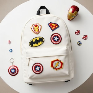 Peut inclure: Un sac à dos blanc orné d'écussons de super-héros, dont Iron Man, Superman, Batman, Captain America et Flash. Des accessoires sur le thème des super-héros, comme un porte-clés et un casque Iron Man miniature, sont également présents.