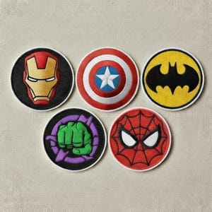 May include: Set of five embroidered patches featuring iconic superhero symbols. Includes Iron Man's mask, Captain America's shield, Batman's bat symbol, Hulk's fist, and Spider-Man's mask. Each patch is circular with a black border and vibrant colors.