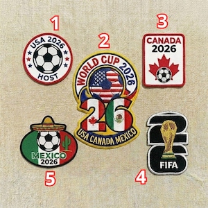 Op de afbeelding: Een verzameling geborduurde patches met voetbalontwerpen en tekst gerelateerd aan het Wereldkampioenschap 2026. Ontwerpen omvatten vlaggen van de VS, Canada en Mexico, samen met de FIFA-trofee.