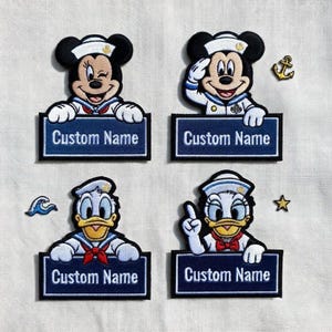 Puede incluir: Cuatro parches bordados con personajes de Disney con trajes de marineros. Se muestran Mickey y Minnie Mouse, y Donald y Daisy Duck. Cada parche tiene un rectángulo azul con las palabras "Custom Name". Se incluyen adornos adicionales con temática náutica.