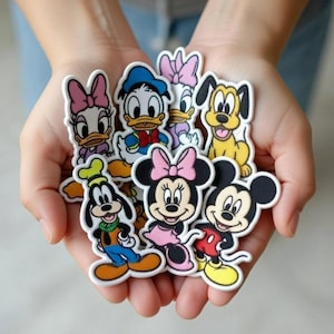 Op de afbeelding: Een verzameling kleurrijke Disney-personage patches, waaronder Mickey Mouse, Minnie Mouse, Donald Duck, Daisy Duck, Goofy en Pluto. Elke patch heeft een witte rand en levendige kleuren, perfect voor het versieren van kleding of accessoires.
