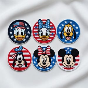 May include: Set of six round embroidered patches featuring Disney characters Donald Duck, Daisy Duck, Pluto, Goofy, Minnie Mouse, and Mickey Mouse. Each patch has a patriotic theme with red, white, and blue colors, stars, and stripes.