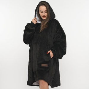 Op de afbeelding: Een zwarte oversized hoodie met een grote zak aan de voorkant. De hoodie heeft een witte voering en een capuchon met trekkoord.