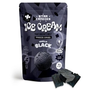 Op de afbeelding: Een zak met gevroren gedroogd vanille-ijs. De zak is zwart met witte tekst die "Star Candies Ice Cream That Doesn't Melt Freeze-Dried Vanilla Black" zegt. De zak heeft ook een afbeelding van een bolletje zwart ijs. De zak ligt op een wit oppervlak met een paar stukjes zwart ijs ervoor.