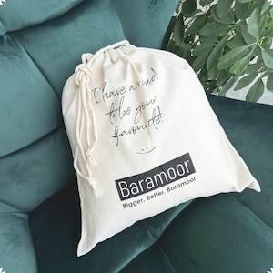 Pu&ograve; includere: Una borsa di cotone bianco con coulisse, con il testo "I have arrived to be your favourite!" e il logo "Baramoor Bigger. Better. Baramoor." stampato in nero.