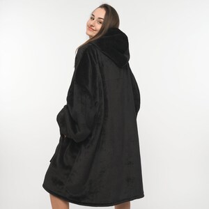 Peut inclure: Une grande couverture &agrave; capuche noire avec une texture douce et moelleuse. La couverture est port&eacute;e par une personne et a une grande capuche.