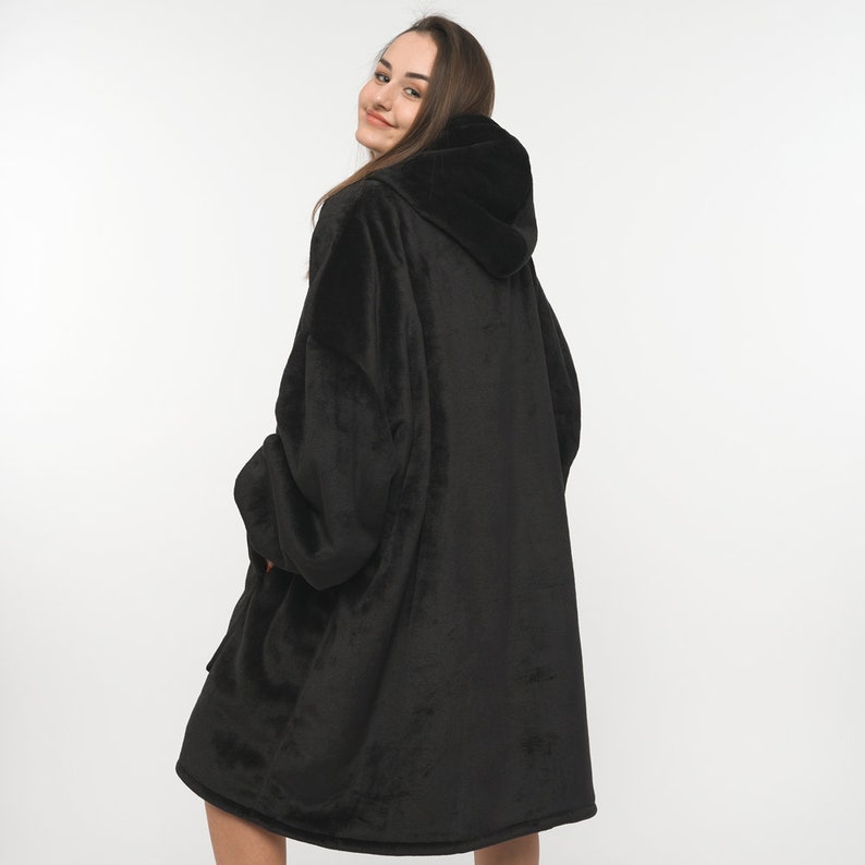 Peut inclure: Une grande couverture &agrave; capuche noire avec une texture douce et moelleuse. La couverture est port&eacute;e par une personne et a une grande capuche.