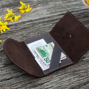 May include: A brown leather wallet with a flap closure, open to reveal a receipt and several bills. The wallet is lying on a wooden surface.
