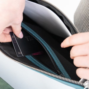 May include: A teal leather clutch purse with a zipper closure. The purse is open and a credit card and passport are visible inside.