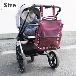May include: A burgundy leather diaper bag with a zipper closure and two straps. The bag is hanging from the handle of a stroller. The bag measures 16 inches tall, 11.8 inches wide, and 16 inches deep.