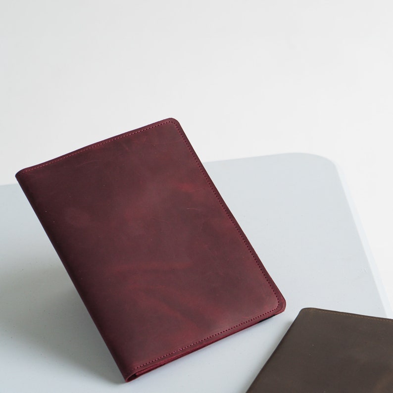Puede incluir: Una cubierta de cuaderno de cuero burdeos con un borde cosido.