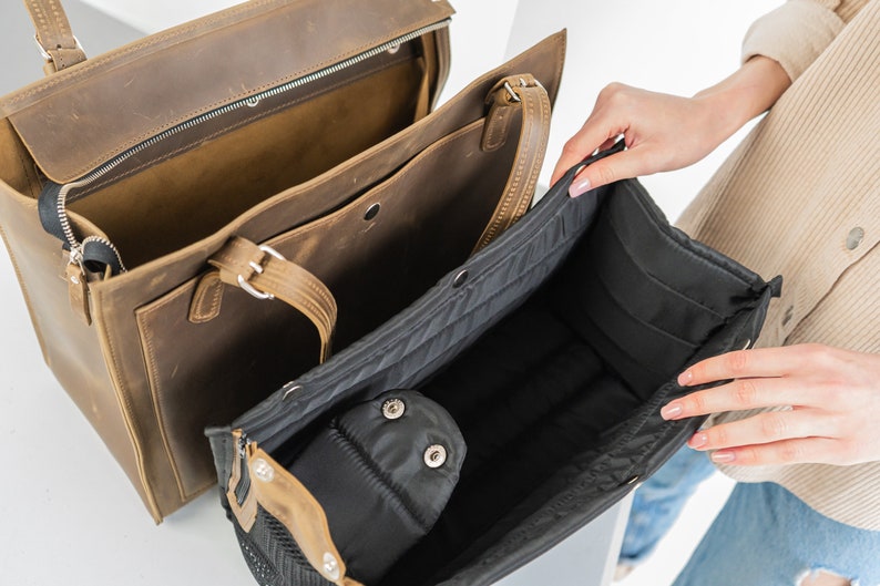 Pu&ograve; includere: Una borsa tote in pelle marrone con una cerniera nera e un interno nero e marrone. La borsa &egrave; aperta e l'interno &egrave; visibile. La borsa ha una tasca con cerniera nera all'interno.