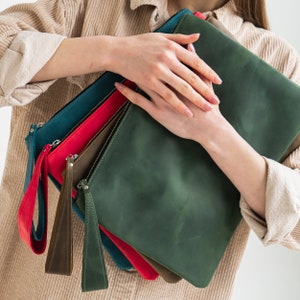 May include: A set of four leather clutches in different colors, including green, blue, red, and brown. The clutches are stacked on top of each other and have a zipper closure.