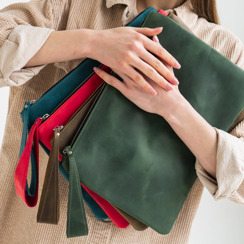 May include: A set of four leather clutches in different colors, including green, blue, red, and brown. The clutches are stacked on top of each other and have a zipper closure.