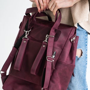 May include: A burgundy leather backpack with adjustable straps and multiple pockets. The backpack has a zippered front pocket and a flap closure.