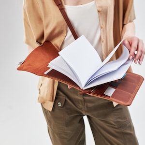 May include: A brown leather journal with a strap and a white notebook inside. The journal is open and the pages are fanned out.