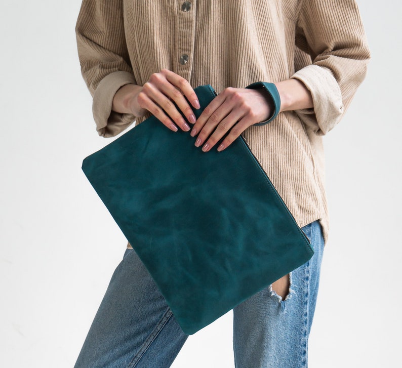 May include: A teal blue leather clutch purse with a smooth, textured surface.