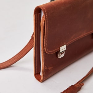 May include: A brown leather briefcase with a silver clasp and a long strap. The briefcase has a flap that closes with a buckle.