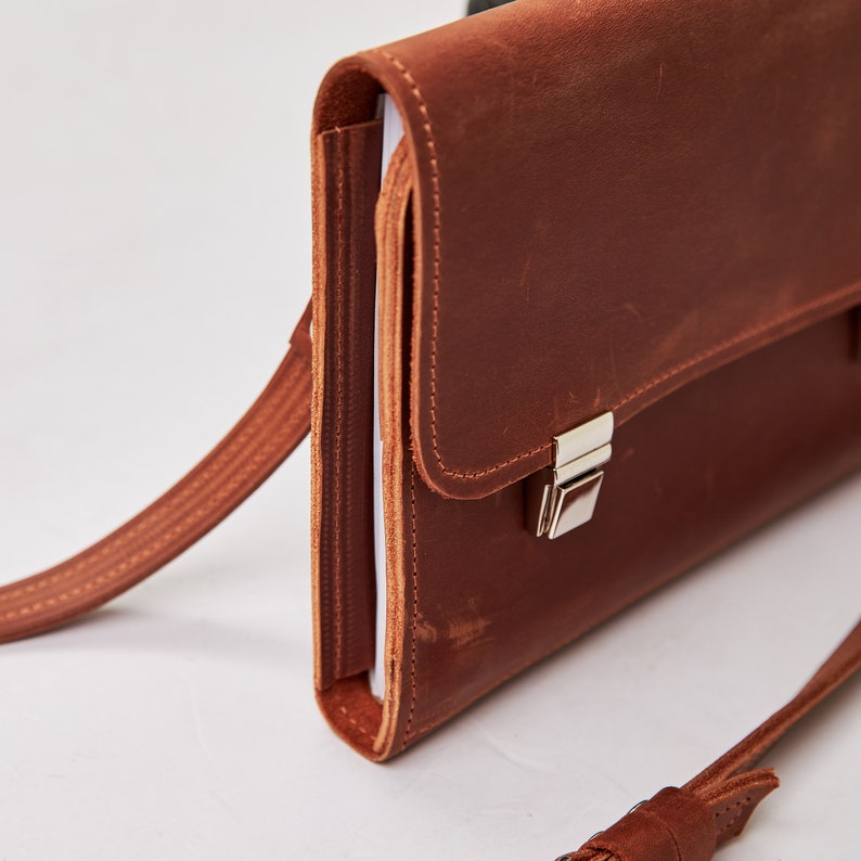 May include: A brown leather briefcase with a silver clasp and a long strap. The briefcase has a flap that closes with a buckle.