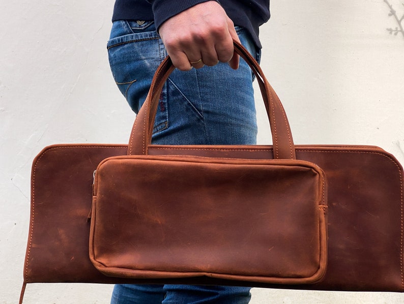May include: A brown leather carrying case with a zippered pocket and two handles.