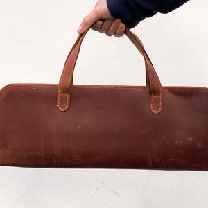 May include: A brown leather carrying case with two handles. The case has a zipper closure and is made of a distressed leather.