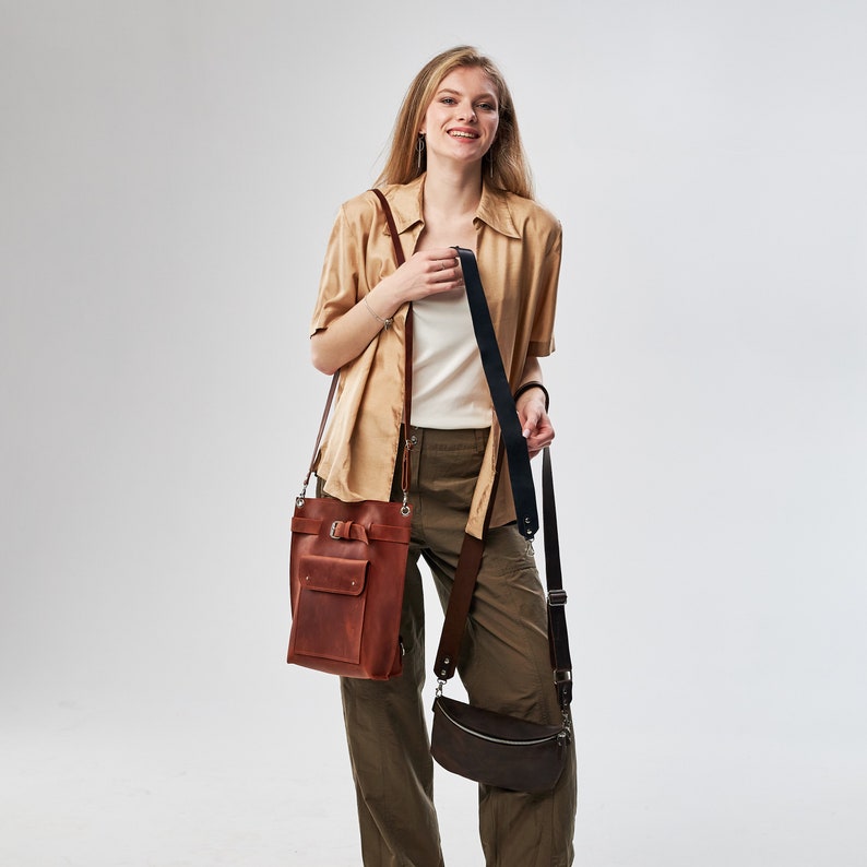 Puede incluir: Una mujer con una camisa marr&oacute;n claro y pantalones caqui lleva dos bolsos de cuero. Uno de los bolsos es marr&oacute;n y el otro es negro.
