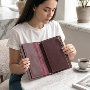 May include: A dark plum-colored leather organizer wallet featuring a tri-fold design, multiple interior card slots, and a vertical zippered pocket. The interior displays a smooth, matte finish with visible stitching along the edges and a metal zipper pull.