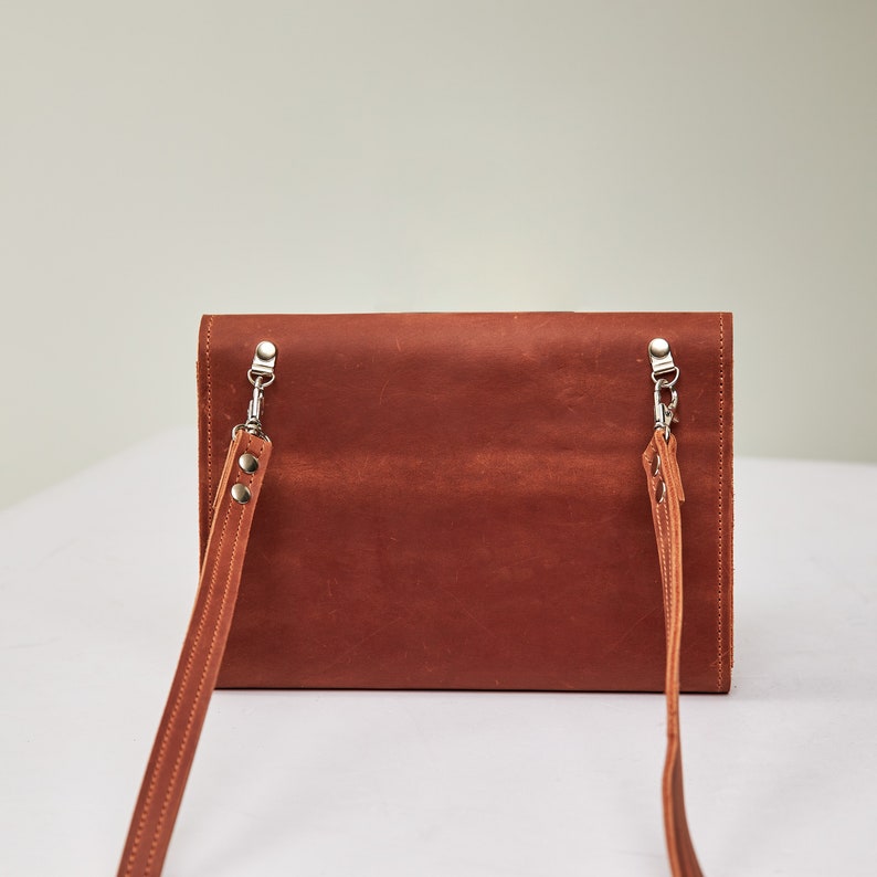 May include: A brown leather crossbody bag with a long adjustable strap. The bag has a flap closure and silver hardware.