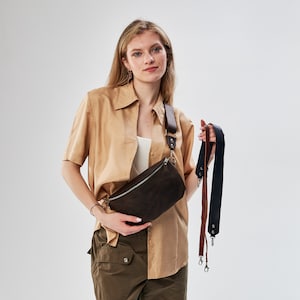 Puede incluir: Una ri&ntilde;onera de ante marr&oacute;n con cierre de cremallera y hebilla plateada. La bolsa la lleva una persona que lleva una camisa beige y pantalones cargo verdes. La bolsa est&aacute; unida a una correa marr&oacute;n y negra.