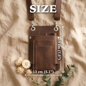 K&ouml;nnte beinhalten: Braune Leder-Umh&auml;ngetasche mit mehreren F&auml;chern, 19 cm hoch und 13 cm breit. Die Tasche hat einen Schulterriemen und Metallbeschl&auml;ge. Das Wort "SIZE" befindet sich oben im Bild.