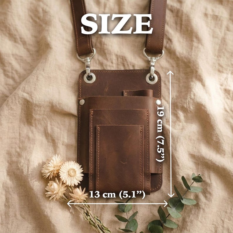 K&ouml;nnte beinhalten: Braune Leder-Umh&auml;ngetasche mit mehreren F&auml;chern, 19 cm hoch und 13 cm breit. Die Tasche hat einen Schulterriemen und Metallbeschl&auml;ge. Das Wort "SIZE" befindet sich oben im Bild.